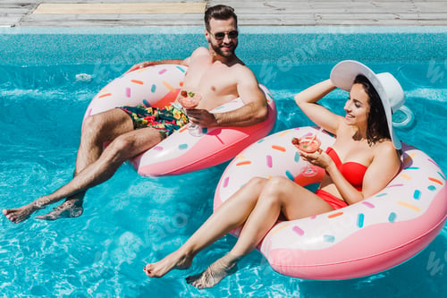 Preview: happy girl in straw hat and handsome man holding cocktail glasses