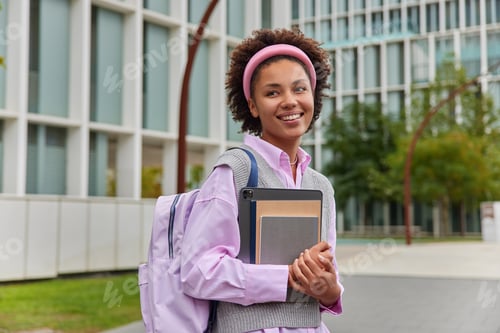 Preview: Outdoor shot of positive teenage girl goes to school in good mood dressed in casual clothes holds no