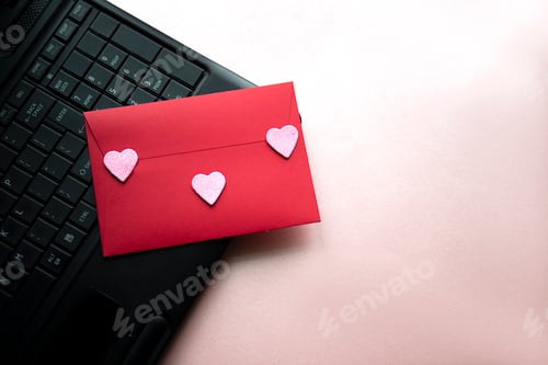 Preview: Love letter in a red envelope with a pink heart on a black laptop keyboard, top view