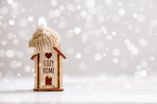 Preview: A small house with a hat stands on a wooden background.