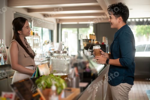 Preview: Young Asian service minded barista with customer in coffee shop