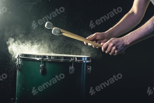 Preview: A man plays a musical percussion instrument with sticks on a dark background.