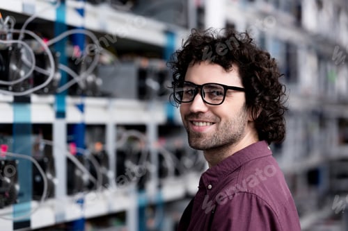 Preview: happy young computer engineer at cryptocurrency mining farm looking at camera