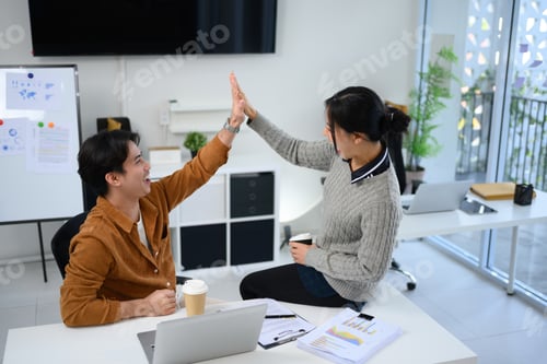 Preview: Cheerful coworkers giving high five to each other celebrating team success in a modern office