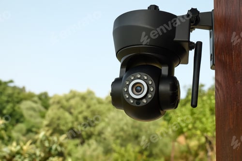 Preview: Security camera on the wall of a building with nature in background.