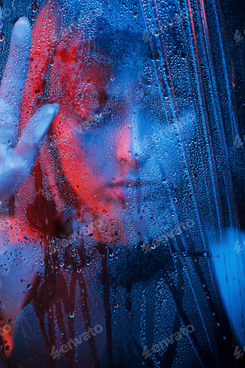 Preview: Studio shot in dark studio with neon light. Portrait of beautiful girl behind wet glass