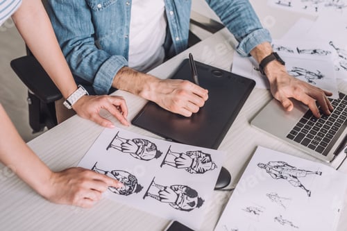 Preview: cropped view of illustrator pointing with finger at cartoon sketch near coworker