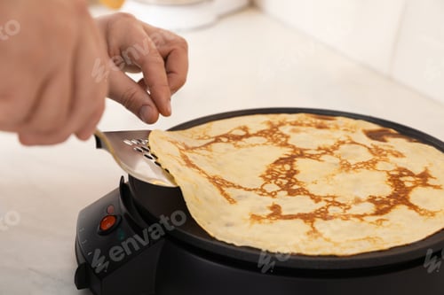 Preview: Man cooking delicious crepe on electric pancake maker in kitchen, closeup