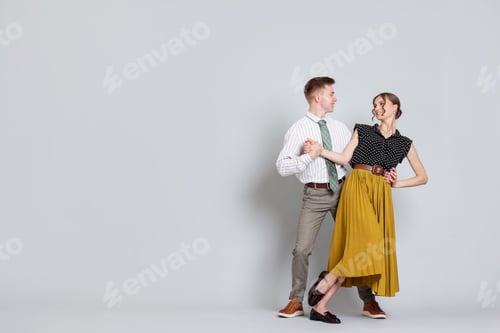 Preview: Happy couple in retro outfits dancing on light grey background, space for text