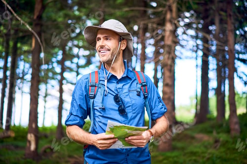 Preview: Smiling man holding a map hiking in the forest