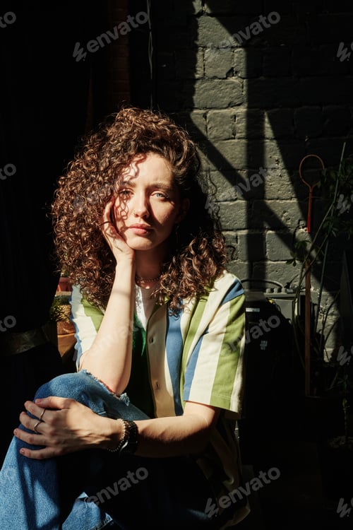 Preview: Young serene female with curly brown hair keeping hand on cheek