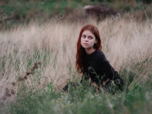 Preview: Red-haired Woman in a black dress lies on dry grass in nature in the forest