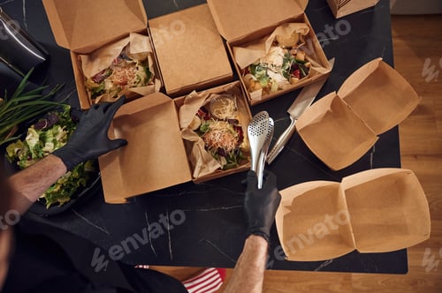 Preview: Top view. Man is packing food into the paper eco boxes. Indoors, restaurant