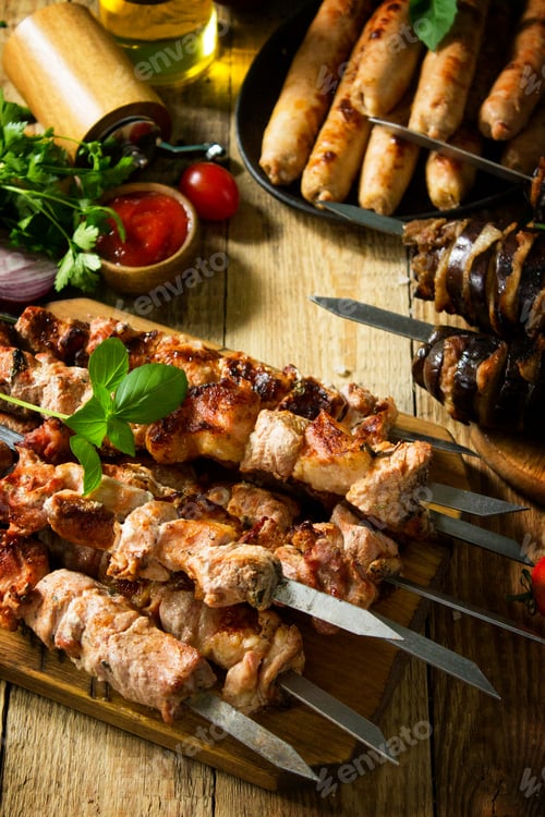 Preview: Grilled meat skewers, grilled sausages and grilled eggplant with bacon on rustic wooden table.