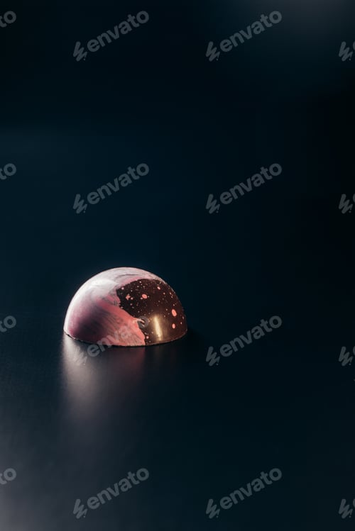 Preview: closeup image of chocolate candy with pink splashes on black background