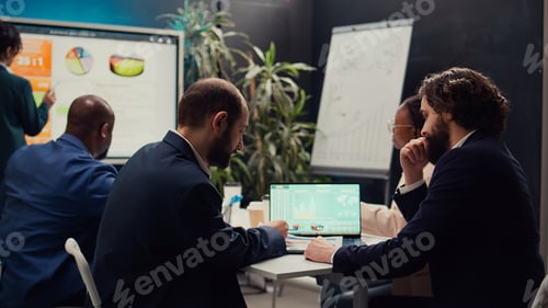Preview: Business partners examining sales infographics in a boardroom