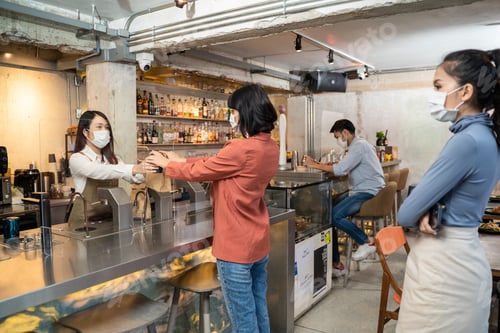 Preview: Woman customer receiving food from waitress with face mask on counter.