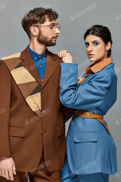 Preview: fashionable couple, models posing in formal attire, looking at camera, grey backdrop, elegant suits