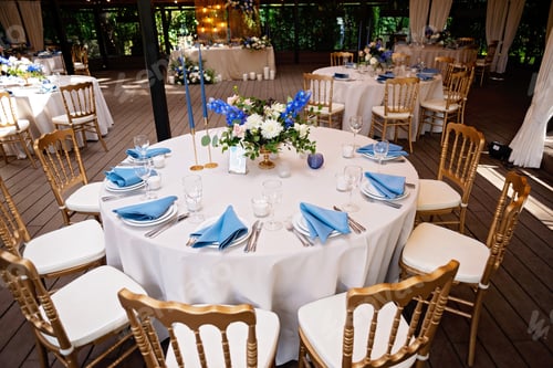 Preview: Festive wedding, table setting with blue linen napkins, candles, golden chairs, and fresh bouquets