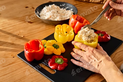 Preview: Woman food blogger preparing stuffed colorful bell peppers with ricotta cheese for Halloween party.