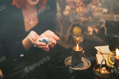 Preview: beautiful red haired young woman in black hat and witch outfit does magic decorated for Halloween