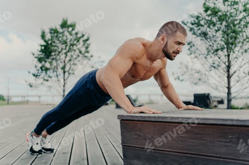 Preview: sportsman in sport wear doing push up outdoors, works on biceps and trains determination