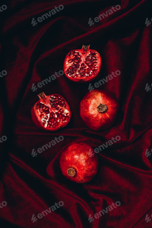 Preview: top view of ripe pomegranates on red velvet fabric backdrop