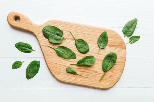 Preview: Wooden cutting board with fresh green spinach salad leaves on white background