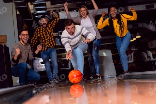 Preview: Group of friends enjoying time together laughing and cheering while bowling at club.