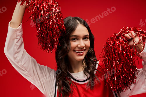 Preview: Fit and stylish young woman celebrating with red pom poms in a vibrant studio space