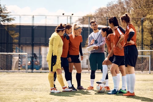 Preview: Soccer coach planning game strategy with female team on playing field.