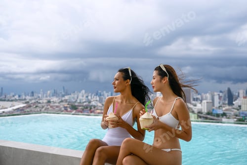 Preview: Female friends spend leisure activity at rooftop swimming pool.