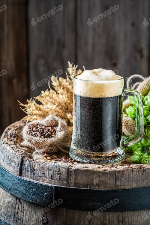 Preview: Fresh pint of dark beer, hops and wheat on old barrel