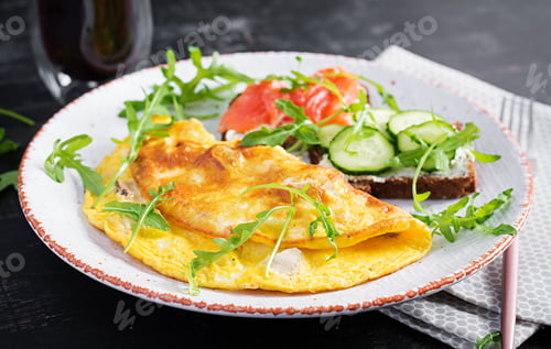 Preview: Omelette with cheese and sandwiches with salmon and cucumber on white plate.