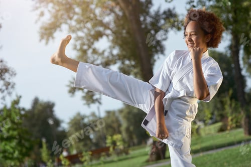 Preview: Joyful little girl in kimono practicing karate on the street
