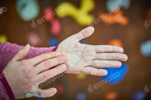 Preview: Climber preparing for ascent with chalked hands in indoor rock climbing gym