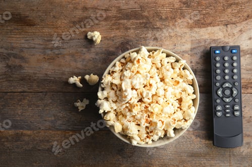 Preview: Bowl of popcorn and TV remote on wooden background, top view with space for text. Watching cinema