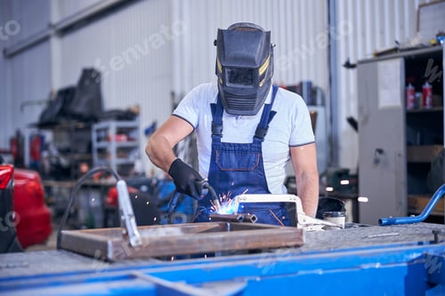 Preview: Male worker in welding helmet welding metal in garage