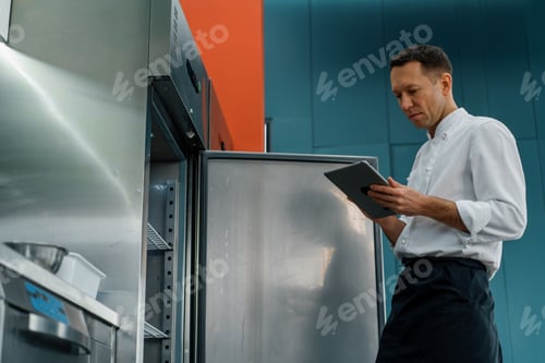 Preview: Professional chef using tablet computer for recipes while working in modern kitchen cooking concept