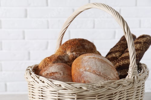Preview: Different types of bread in wicker basket against white brick wall, closeup
