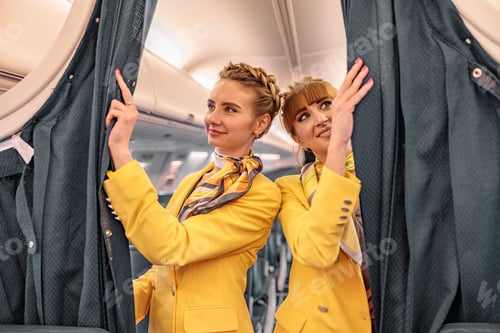 Preview: Joyful flight attendants adjusting curtains in airplane