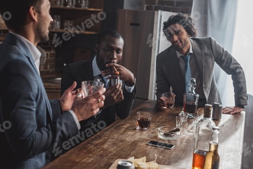 Preview: cropped shot of smiling multiethnic businessmen talking while smoking cigars and drinking whiskey