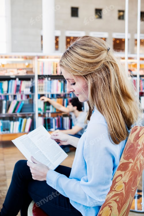 Preview: Side view of young woman reading book in library