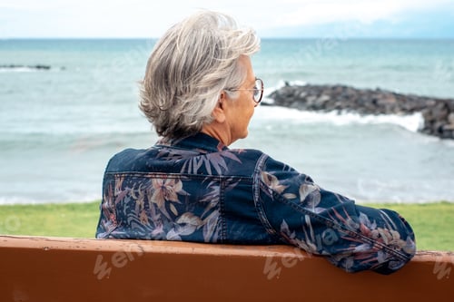 Preview: Back view of senior woman sitting on a bench at the beach enjoying free time vacation retirement