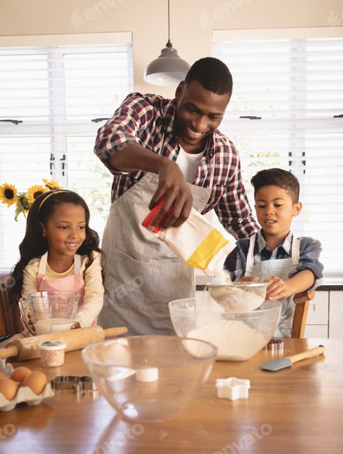 Preview: Front view of African American father and children baking cookies in kitchen at home