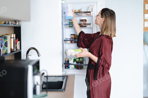 Preview: Woman looking into the fridge at home