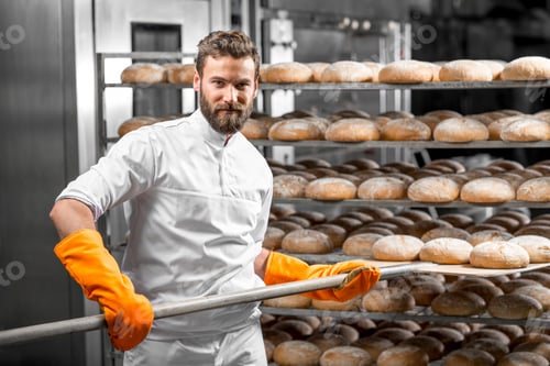 Preview: Baker putting with shovel bread loafs at the manufacturing