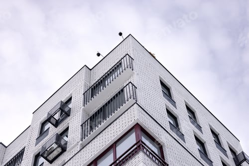 Preview: Corner of a brick apartment building with balconies against the sky.