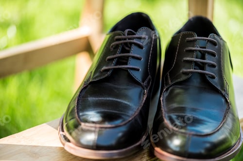 Preview: selective focus of black leather shoes on wooden stairs with green blurred background
