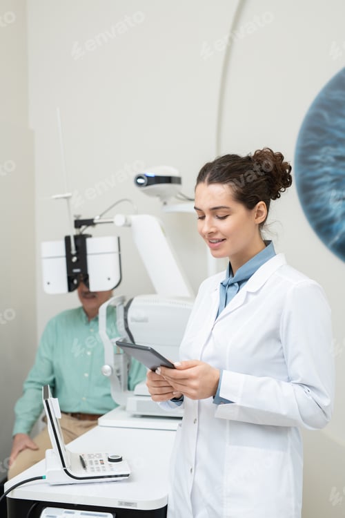 Preview: Happy young female ophthalmologist in whitecoat looking at tablet display